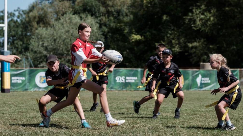 A girl passes the ball whilst playing tag rugby. 