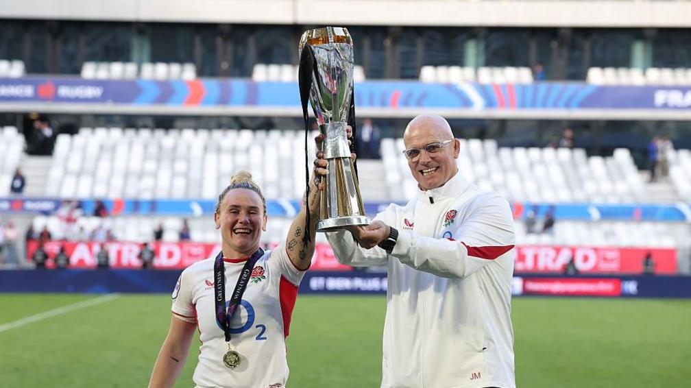 meg jones and John Mitchell standing side by side holding up the six nations trophy together