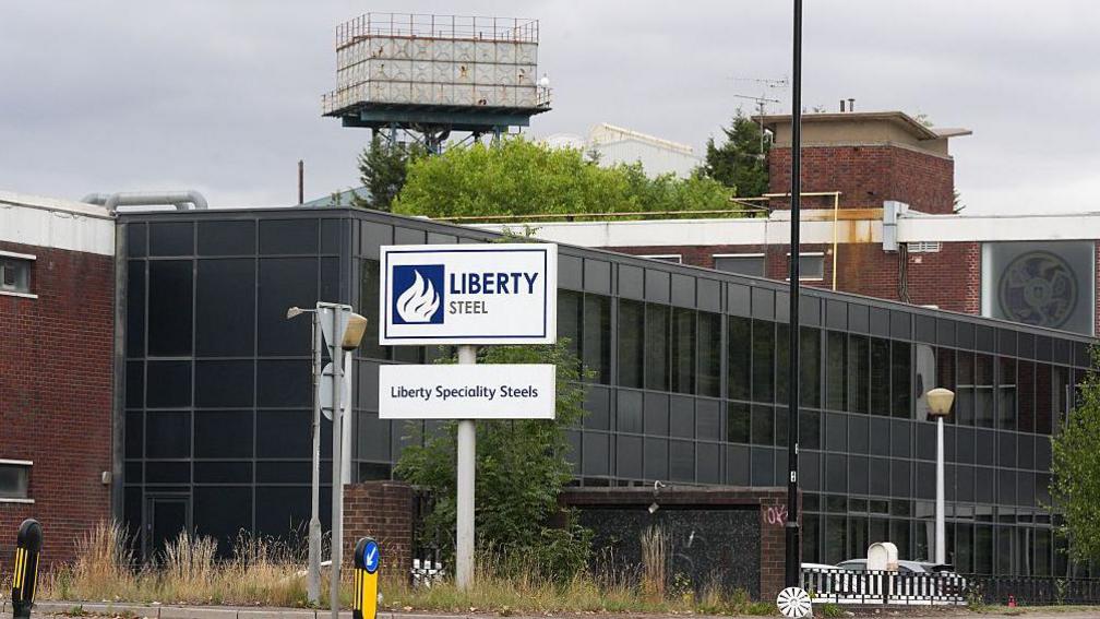 A large black buyilding with gates in front of it it and a large white and blue sign reading Liberty Steel with a smaller sign beneath it reading Liberty Specialty Steels