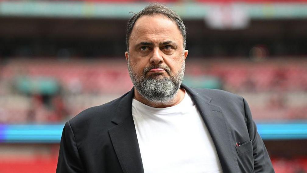 Evangelos Marinakis wearing a black jacket and white t-shirt