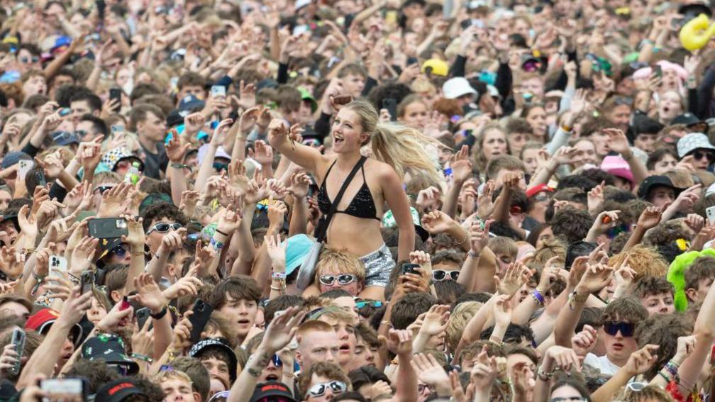 A general view of the crowd during Reading Festival. A woman in the centre of the image is on someone's shoulders.