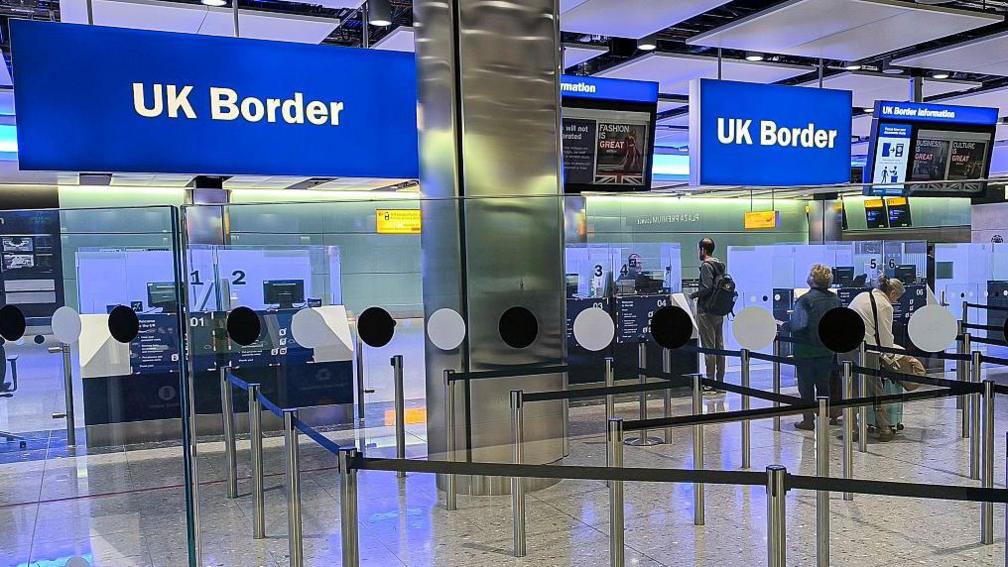 Uk Border at Heathrow airport. two blue signs that read UK border. Below it are the passport control desks