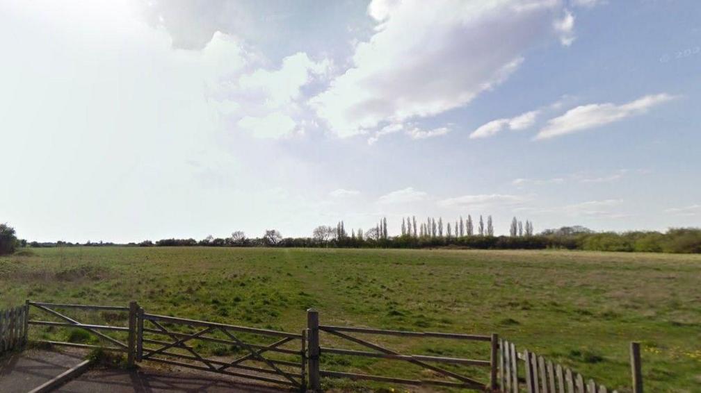 Gates in front of open fields, with trees in the distance and blue sky above