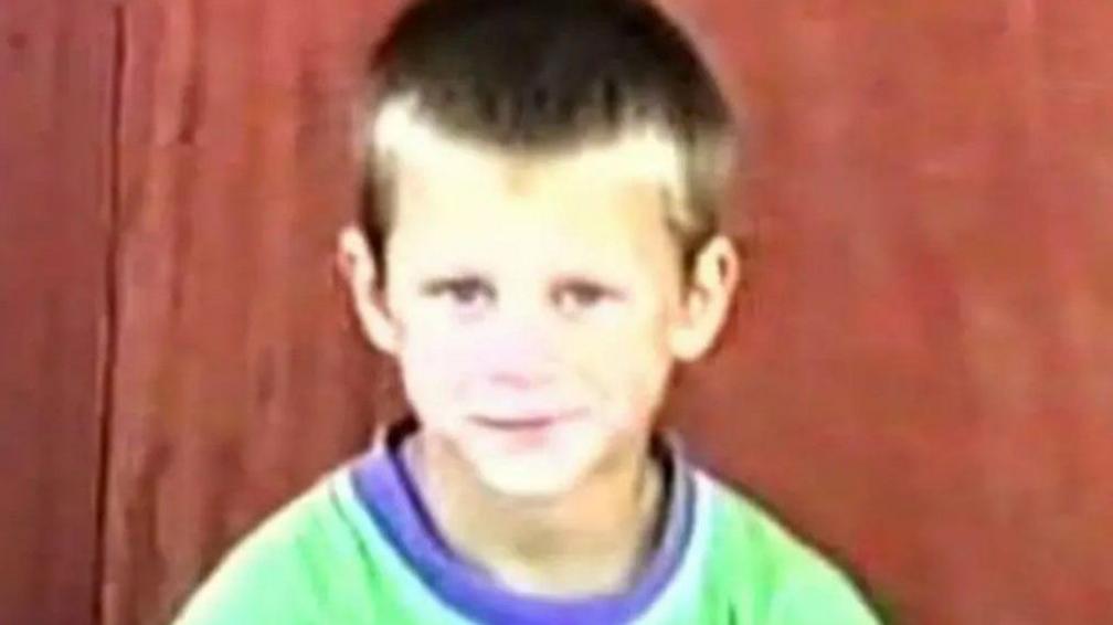 Joe McCafferty, seven, smiling to camera in a blurry photo. He is wearing a green top.