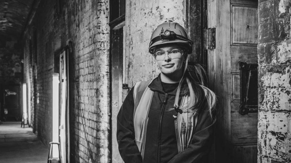 A black-and-white photograph of Leah Finch, a construction manager, leans against a bare wall inside Manchester Town Hall