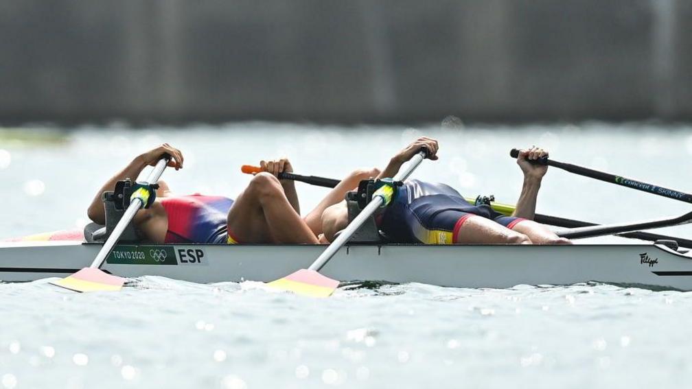 Two rowers lying all the way back on their rowing boat looking exhausted after finishing a race