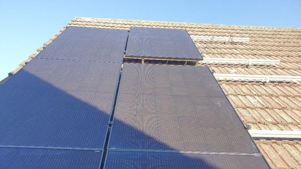 A roof with solar panels on it. There is blue sky behind the roof.