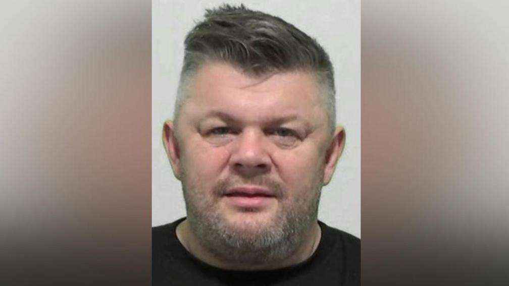 Anthony Craggs' mugshot. He has a grey stubbly beard with short dark hair swept over to the right and shaved grey sides.