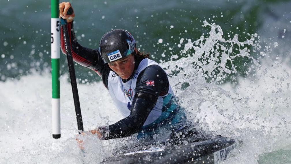 Mallory Franklin competing at the Paris Olympics, with water hitting her canoe as she paddles around a post 