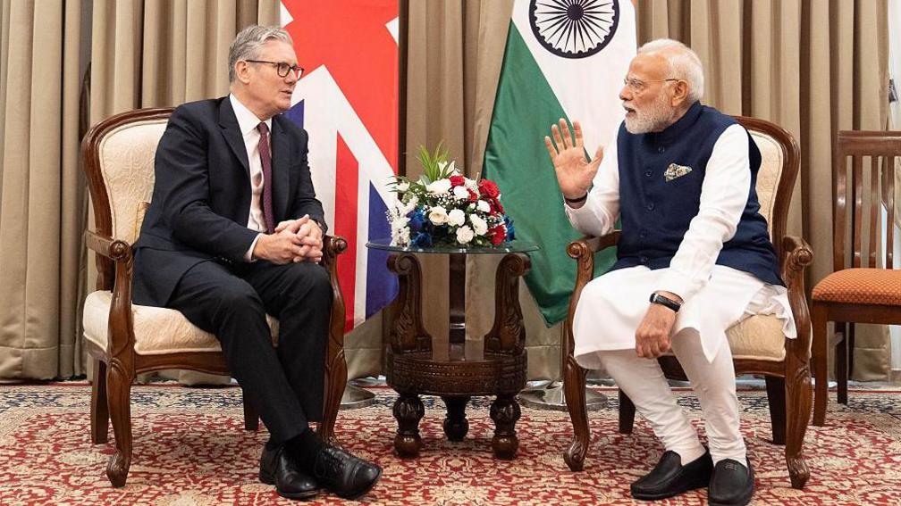 Kryeministri Sir Keir Starmer dhe Kryeministri i Indisë Narendra Modi në një takim dypalësh në Mumbai, Indi në tetor 2025. Pas tyre janë flamujt e të dy vendeve. Kryeministri Keir Starmer udhëtoi së bashku me përfaqësues nga bizneset, universitetet dhe institucionet kulturore britanike për të promovuar marrëveshjen e tregtisë së lirë të nënshkruar midis Mbretërisë së Bashkuar dhe Indisë.