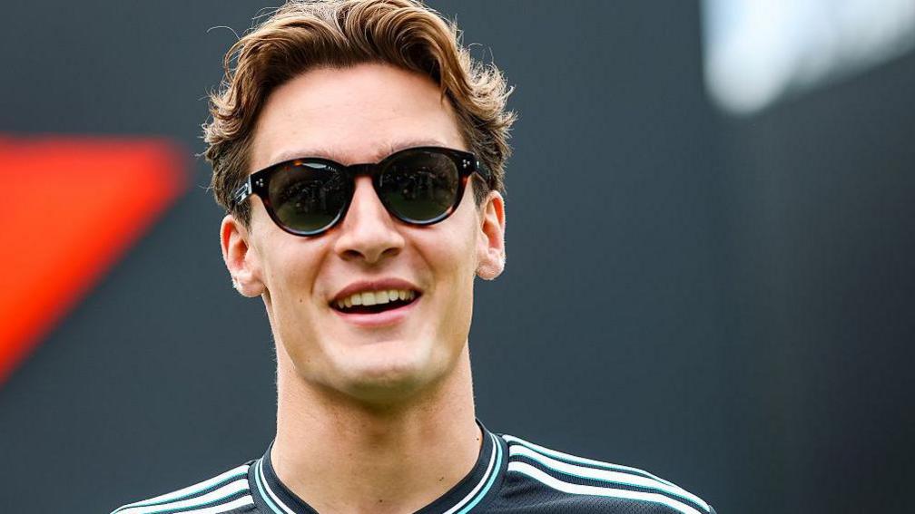 George Russell smiling while wearing sunglasses