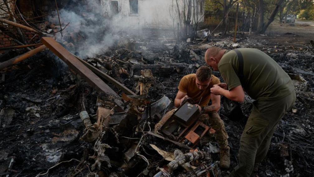 Ukrainian servicemen examine the wreckage of a downed Russian aircraft, likely a Sukhoi S-70 "stealth" heavy unmanned combat aerial vehicle (UCAV), which crashed in a residential area, setting a house on fire on October 5, 2024 in Kostyantynivka, Ukraine