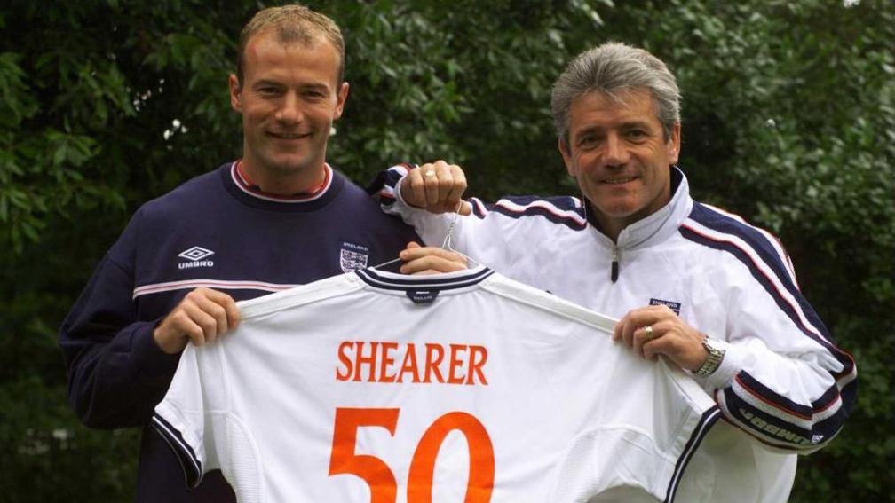 Alan Shearer and Kevin Keegan both hold an England shirt which reads 'Shearer 50' on the back
