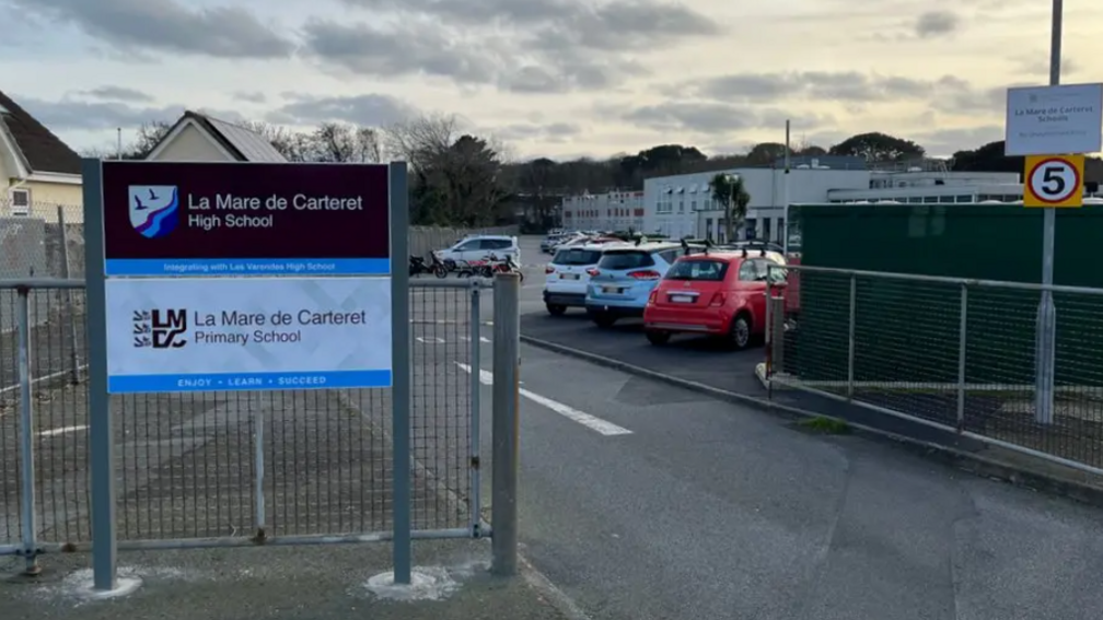 The entrance to La Mare de Carteret school. showing metal gates. parked cares and signage.  