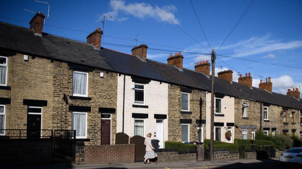 A woman walks down a row of traditional terraced houses in Barnsley