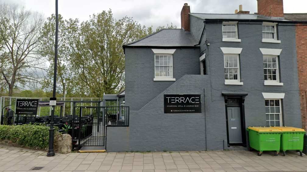 The outside of the Terrace bar. It is a grey building with an outdoor terrace garden, which has glass screens around it.