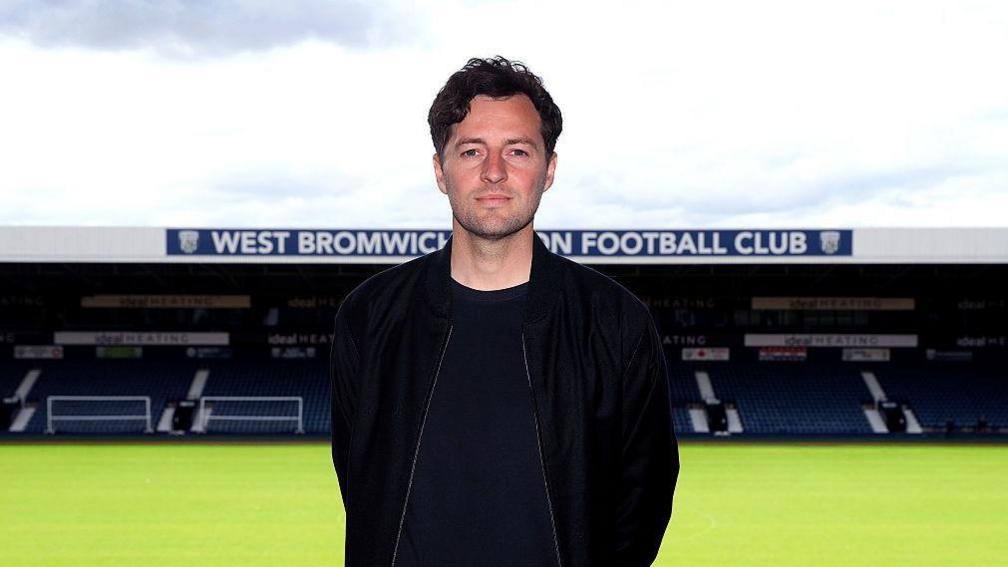 Ryan Mason stands in front of the pitch at The Hawthorns with the stand in the background showing the club's name across the front of its roof