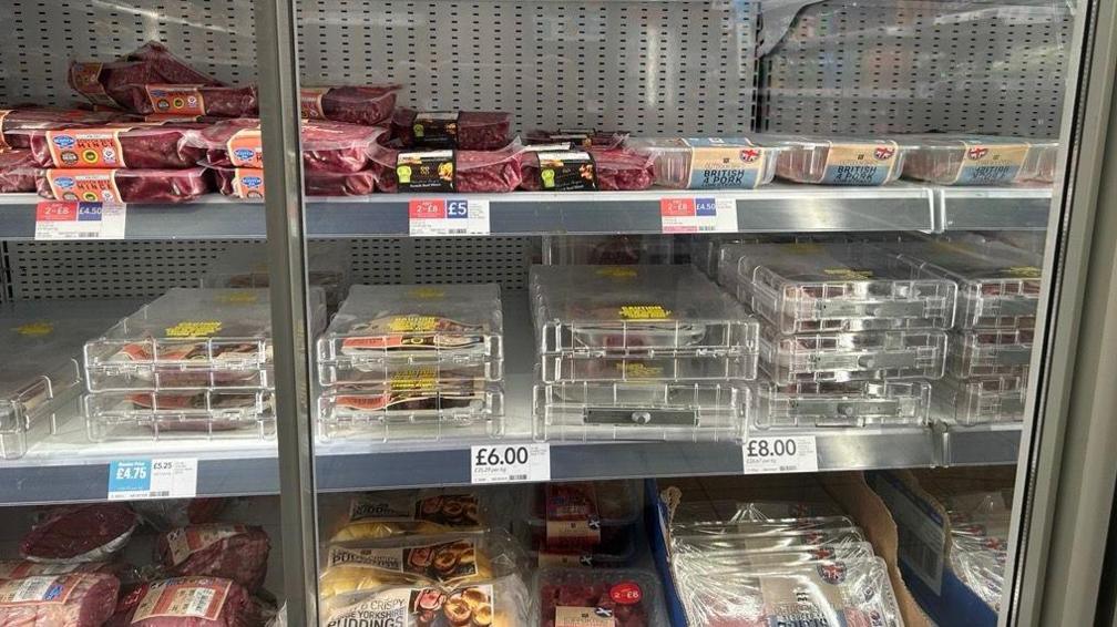 Steaks stacked in think security boxes that are clear in a Co-op.