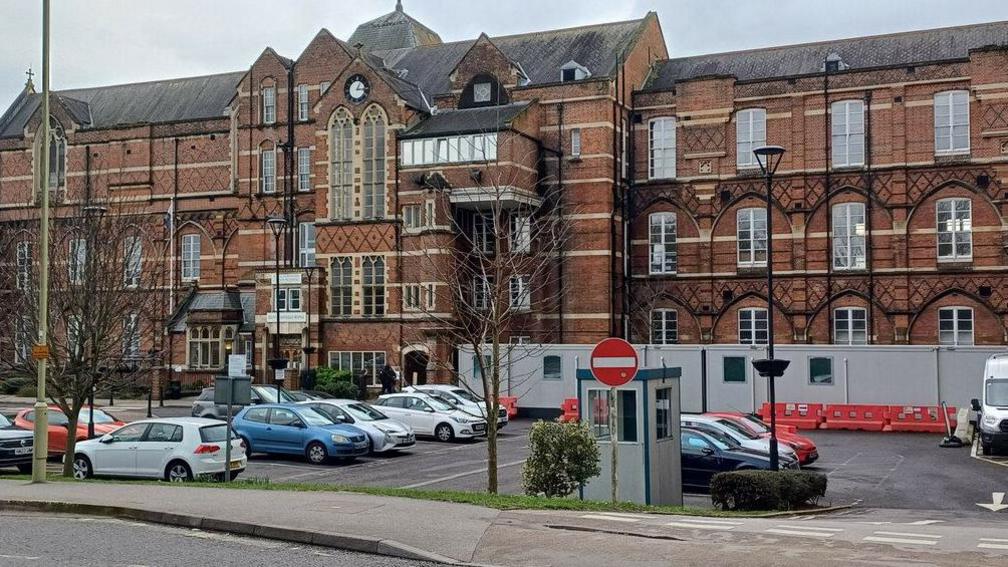 Royal Hampshire County Hospital, a large handsome brown-bricked Victorian building. A car park outside includes some portable cabins.