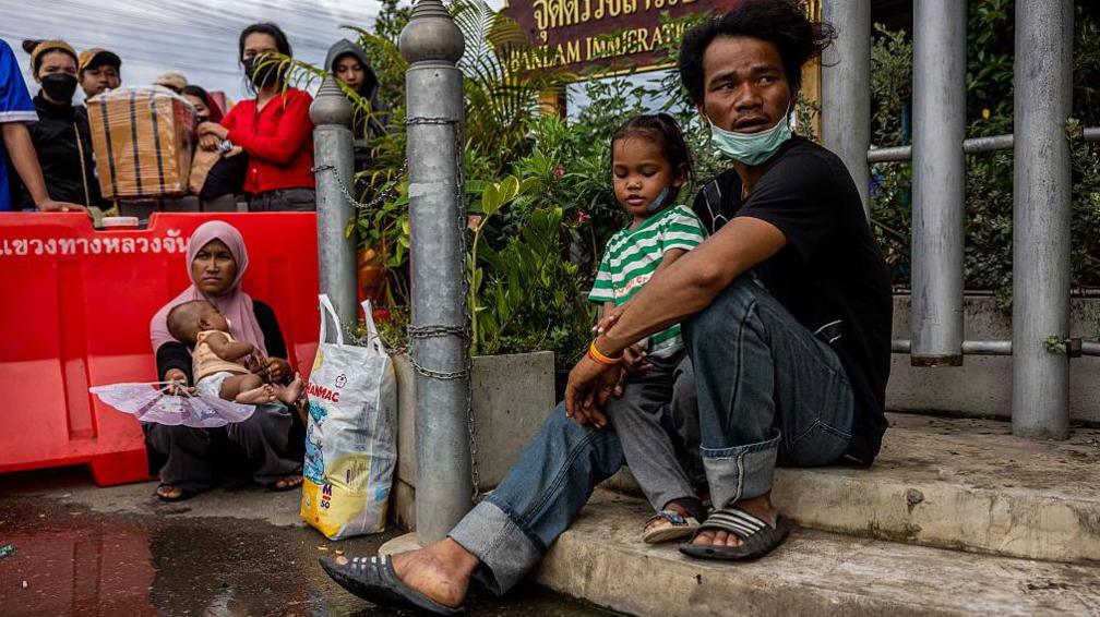 A Cambodian man and woman carry children while waiting to cross the border in Thailand