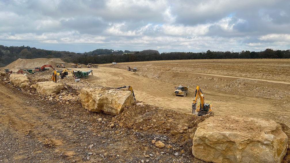 Diggers and machinery are levelling Cotswold stone ahead of building the new roads. The landscape is bare with no vegetation.