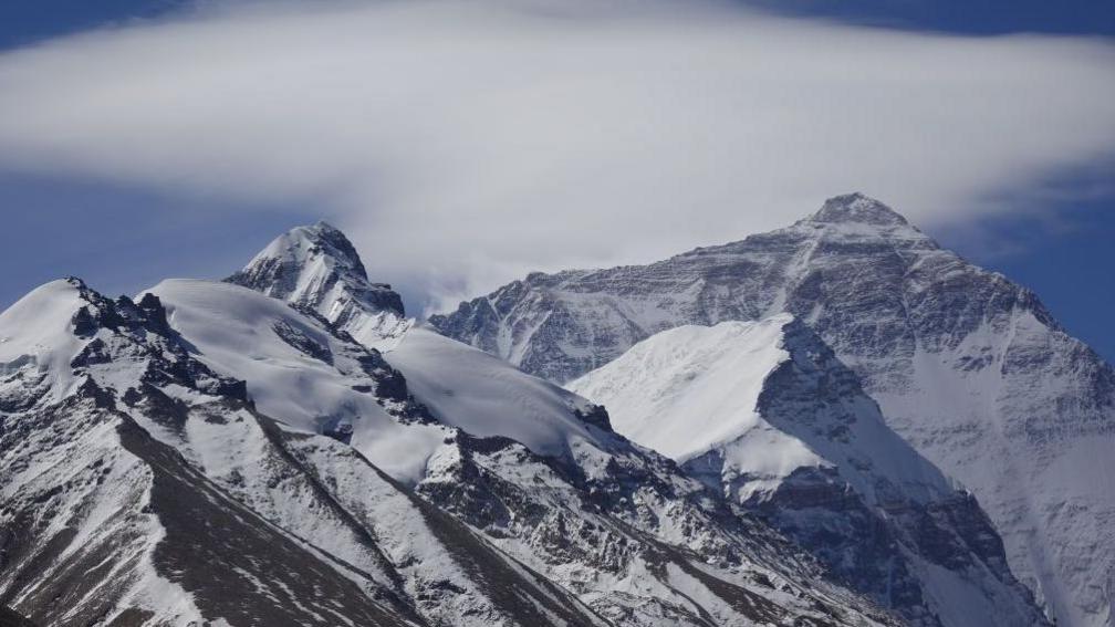 The peaks of Mount Everest covered in snow with a cloudy sky in the background