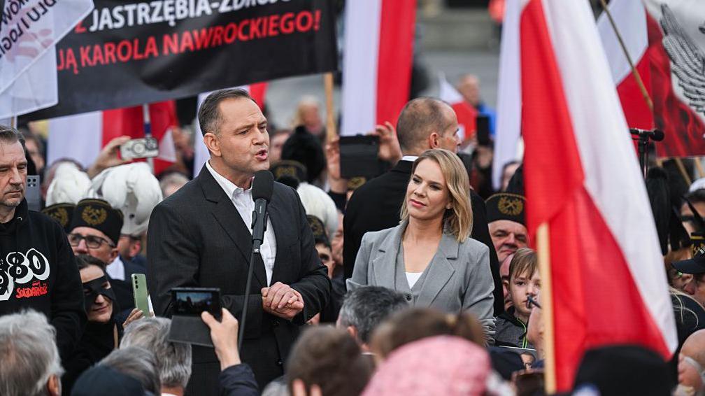 Poland's conservative presidential candidate addresses supporters wearing a black jacket alongside a woman