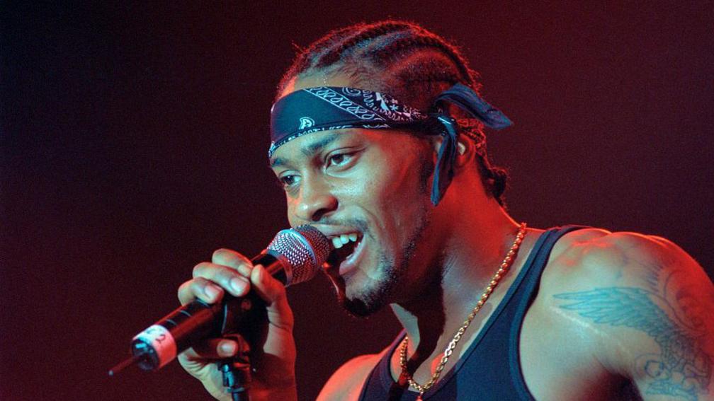 D'Angelo singing into a microphone on stage.