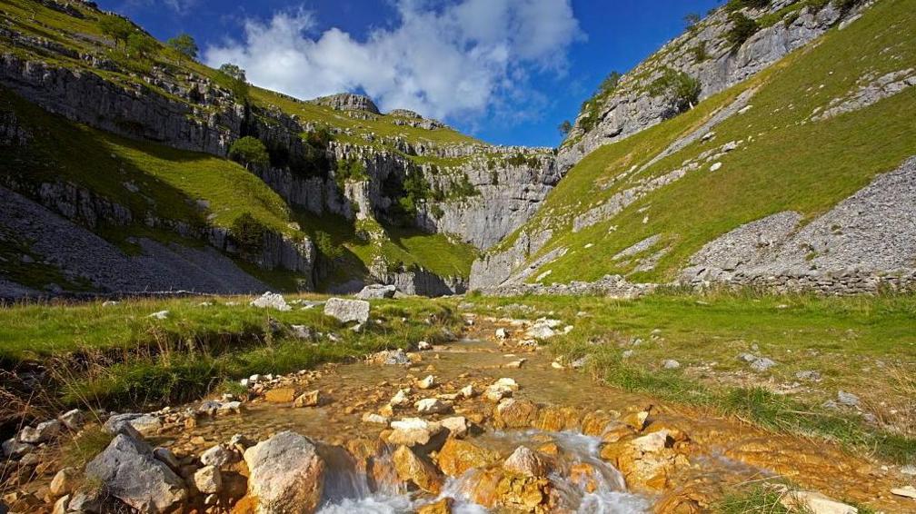 A rock strewn grassy pathy leads to a mountain gorge.