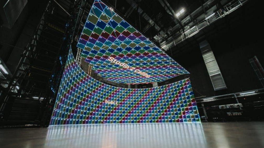The studio space with a green screen made up of a series of of large multi-coloured grids.