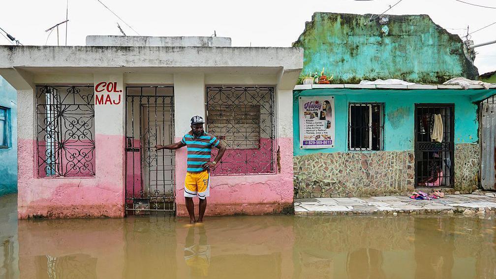 A man stands next to a house on a flooded street after the passing of the tropical storm Melissa before becoming a hurricane at Las Cucarachas neighborhood in Santo Domingo, Dominican Republic on October 28, 2025.