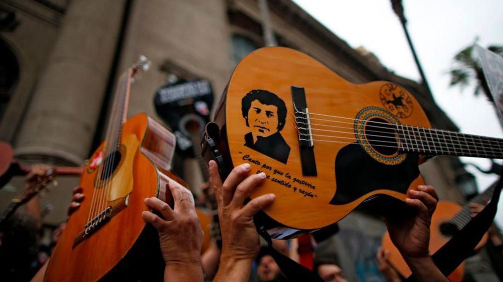 Guitar with a picture of Victor Jara and a quote in Spanish held up during a demonstration in Santiago in 2019