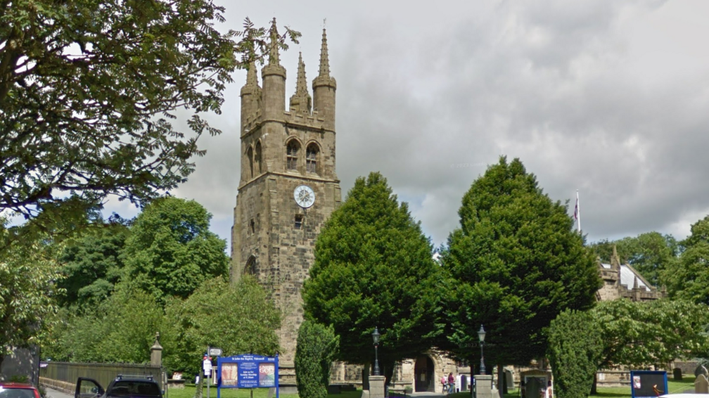 A tall stone medieval church tower with a clock face