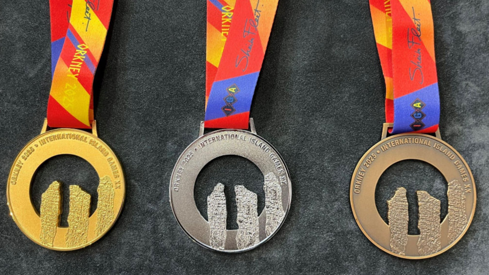 Gold, silver and bronze medals with the shape of three standing stones cut out in a circular piece of metal, on colourful ribbons.