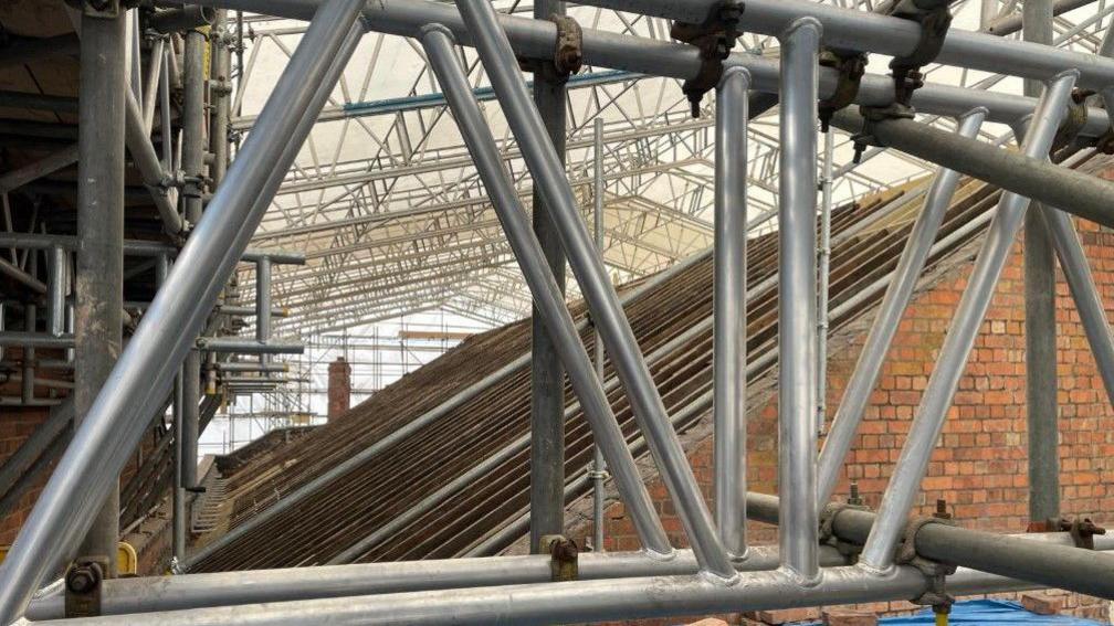The roof, which is at an angle, is pictured side on in the middle and on the right of the photo. The lighter temporary roof is above it.