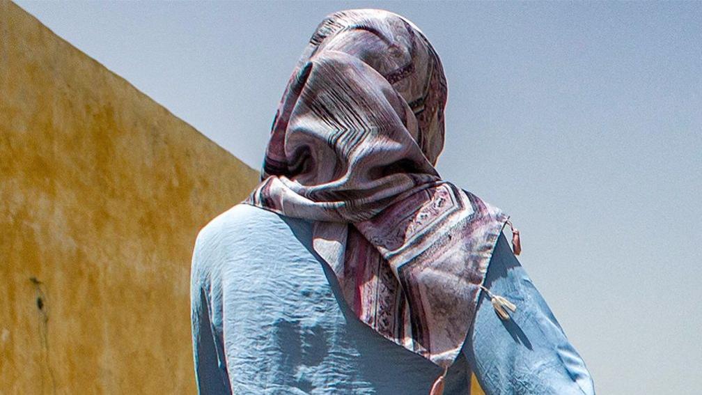 A woman wearing a multi-coloured hijab and a light blue shirt looks away from the camera in the Sudanese state of Gezira 