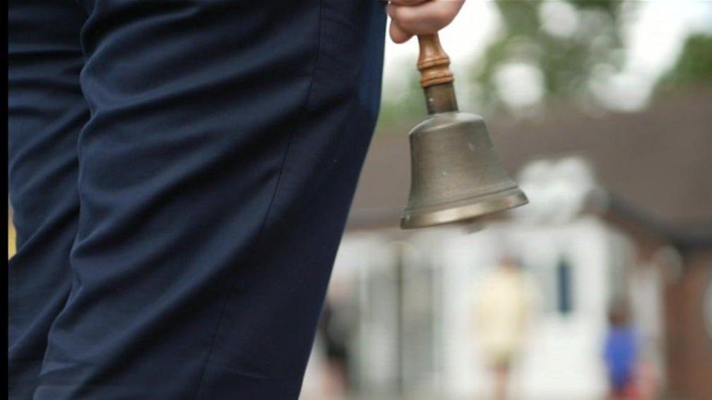 A teacher carrying a school bell