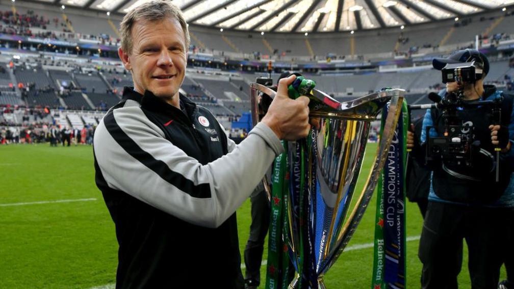 Mark McCall holds aloft the European Champions Cup trophy, which has blue and green ribbons hanging either side