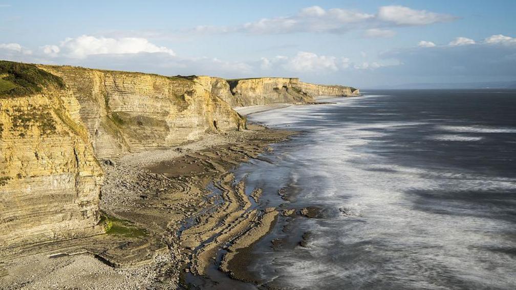 Cliffs to the left, with a pebbly beach below and the sea on the right.