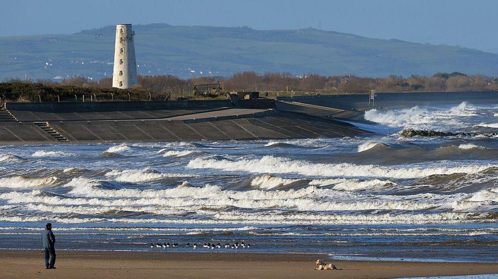 generic images of man walking dog on beach with Leasowe lighthouse in background