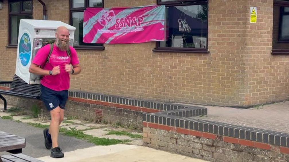 A man looks pleased as he reaches the end of the challenge. He is bald with a large grey beard.