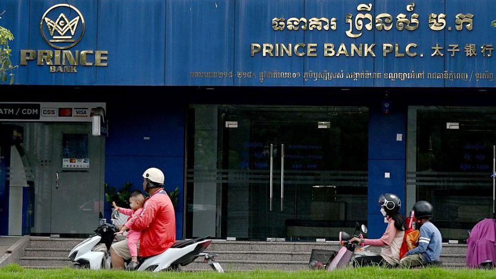 Motorists ride past a branch of the Prince Bank in Phnom Penh on October 15, 2025.