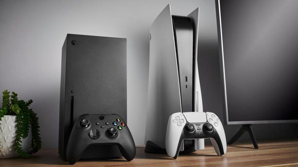 Living room with Microsoft Xbox Series X (L) and Sony PlayStation 5 home video game consoles alongside a television and soundbar.