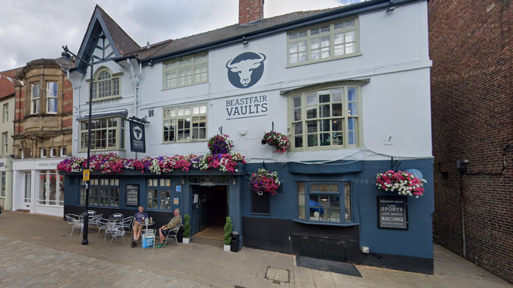 A large old pub painted blue and white with flower displays and a sign reading Beastfair Vaults