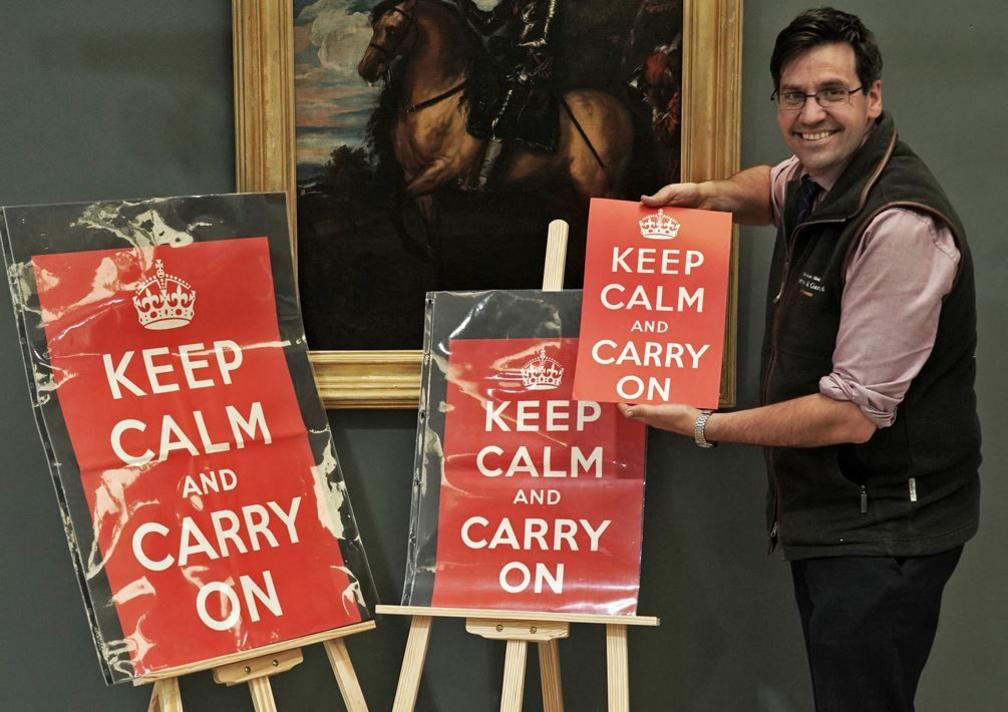 A man holds the smallest poster with the other two displayed on easels