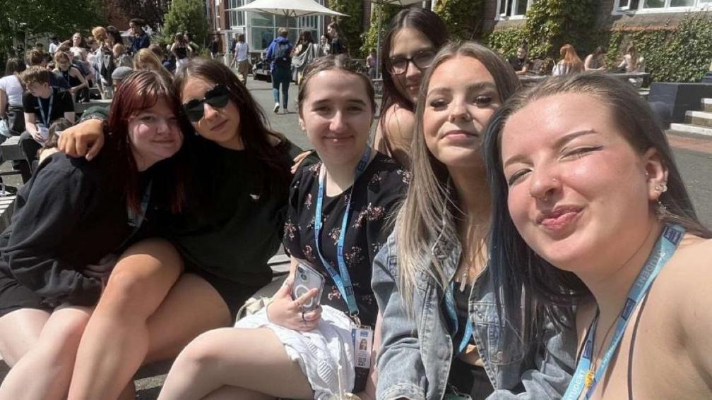 Emily and five friends sitting in the sun outside college