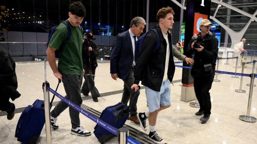 Hugo Auradou (in green) and Oscar Jegou (in light blue shorts) pull luggage though Buenos Aires airport