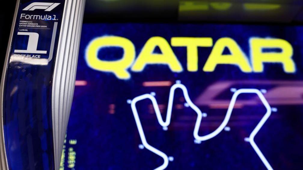 A Formula 1 trophy in front of a sign for the Qatar Grand Prix