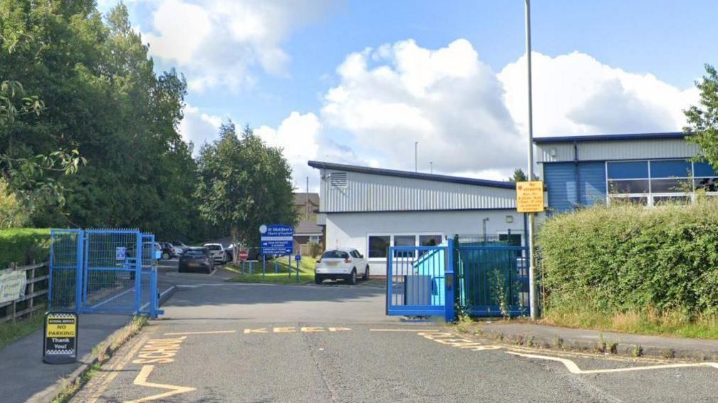 A school with a drive in front and wide blue metal gates 

