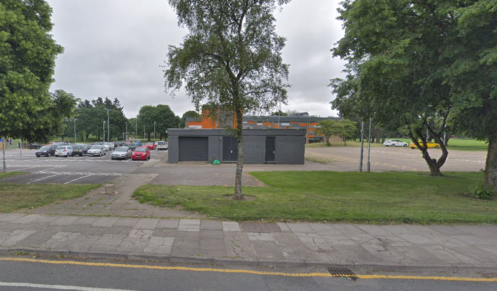 Eastern Leisure Centre in Llanrumney, Cardiff, as seen from the road, with buildings in the background, cars in the car park, and a green area on one side